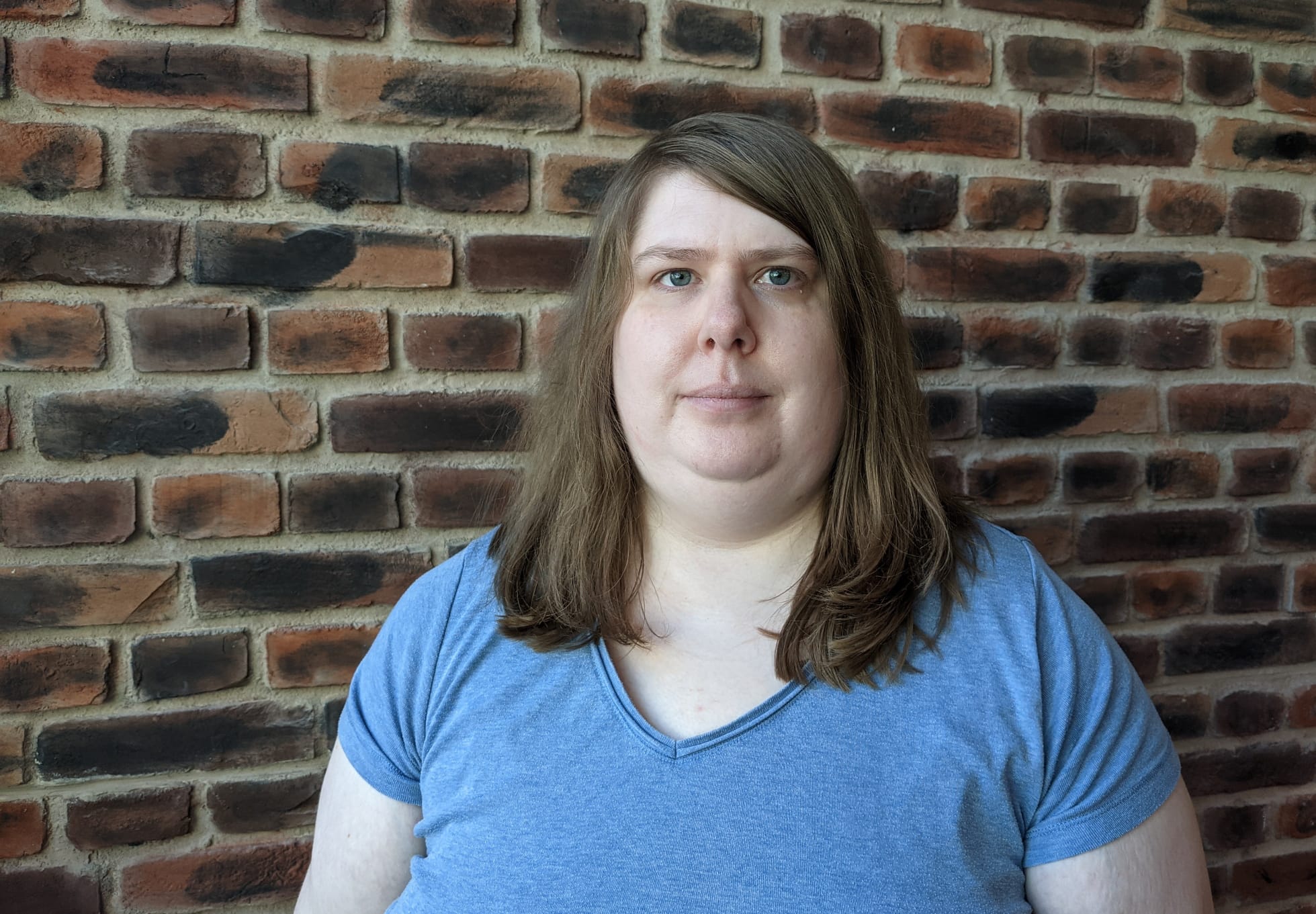 April Slocombe, EI's content volunteer, stands in front of a brick wall.