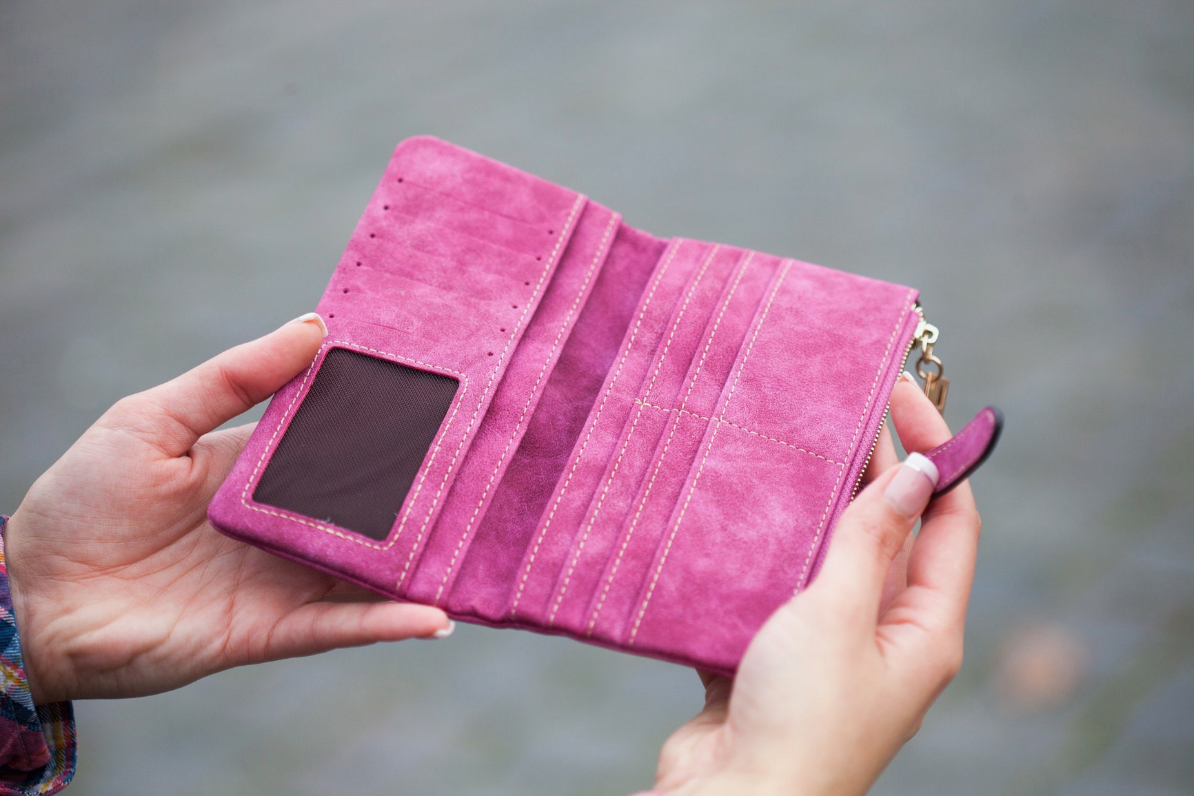 A woman's hands hold open a bright pink purse or wallet.