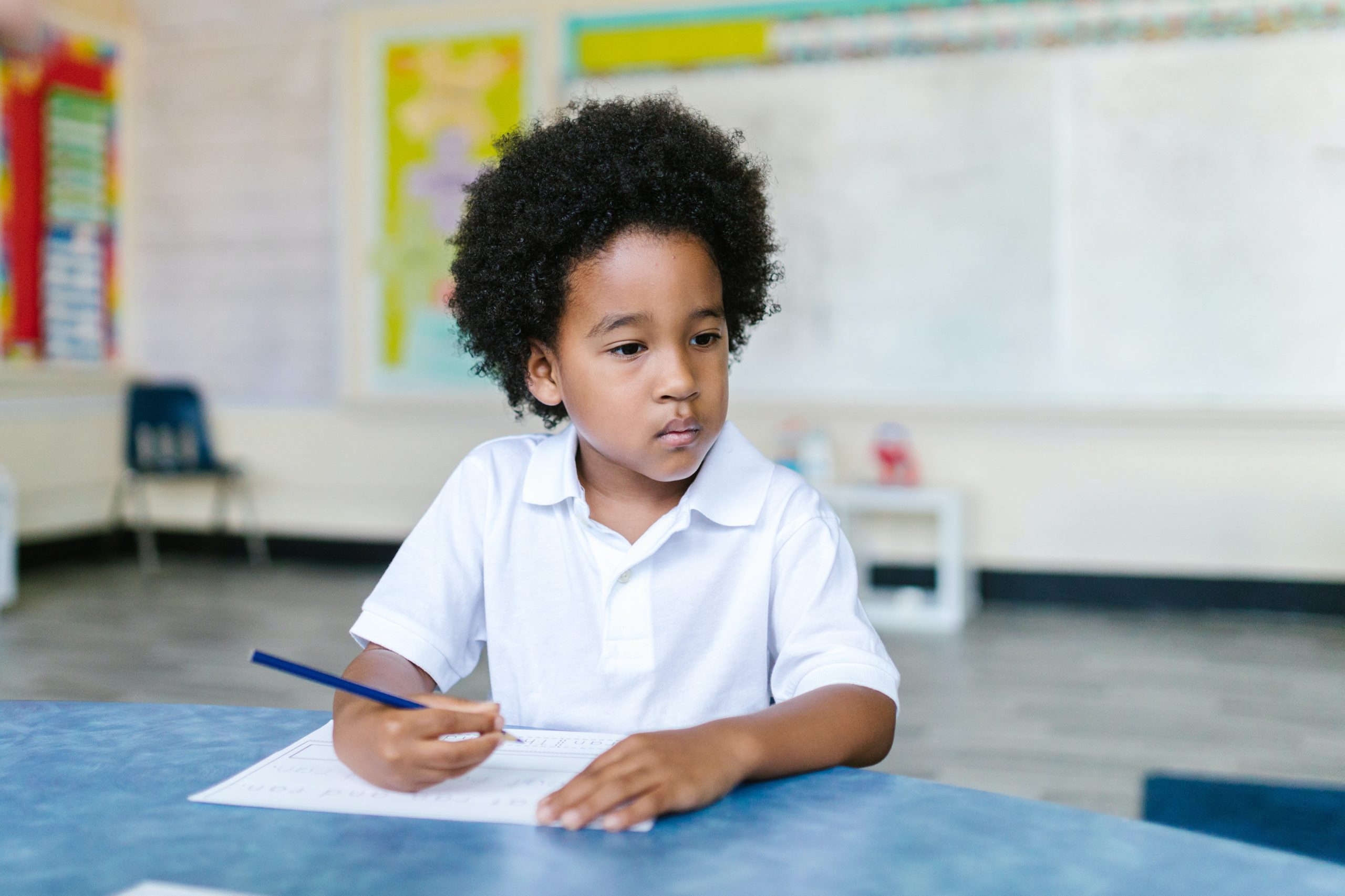 A schoolboy is holding a pen in one hand and looking in the opposite direction.