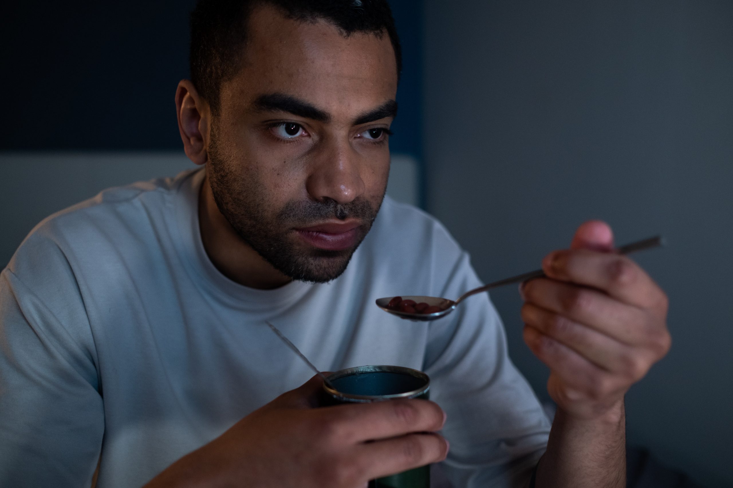 A man is eating a tin of food with a spoon.