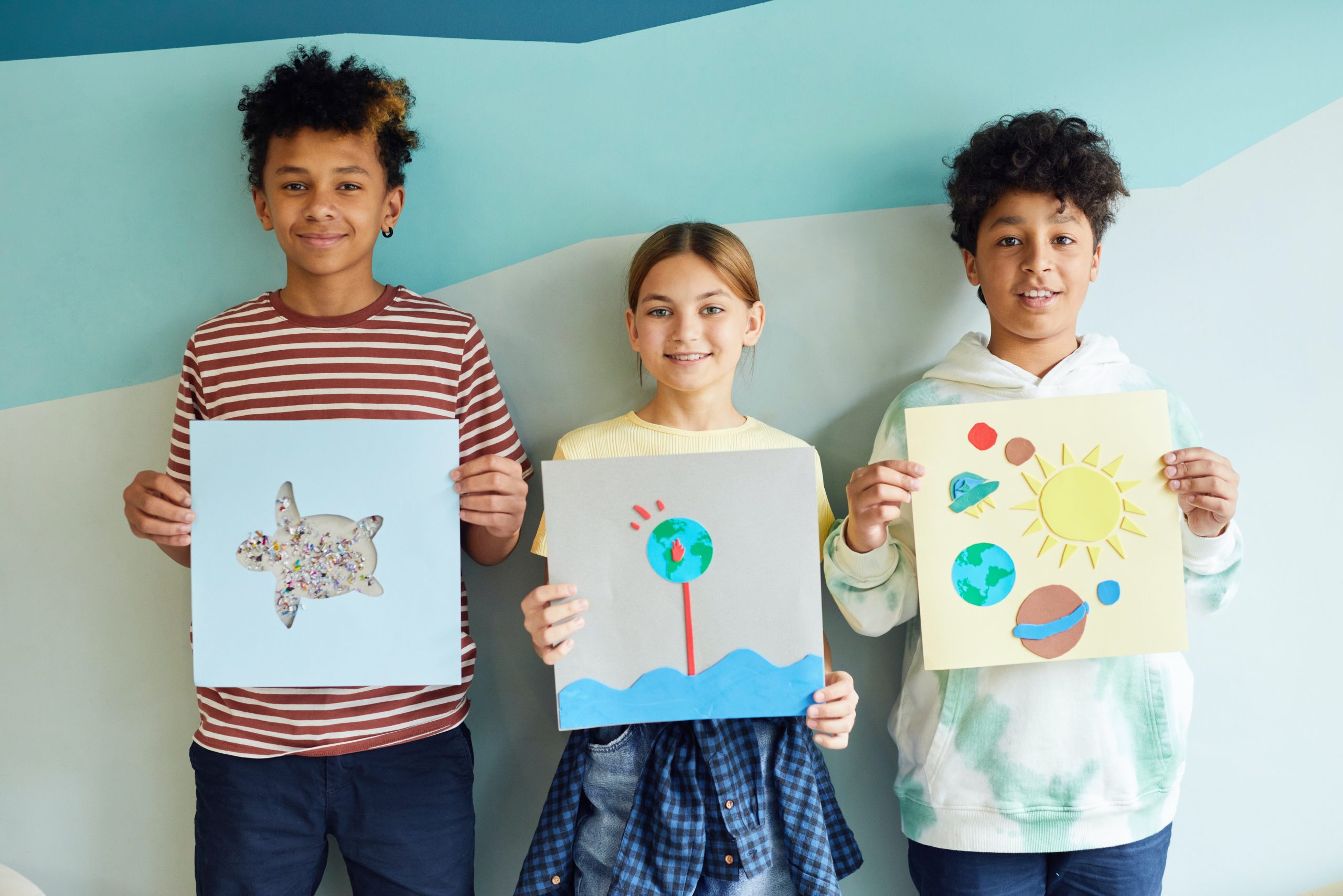 Three smiling children hold up their works of art.