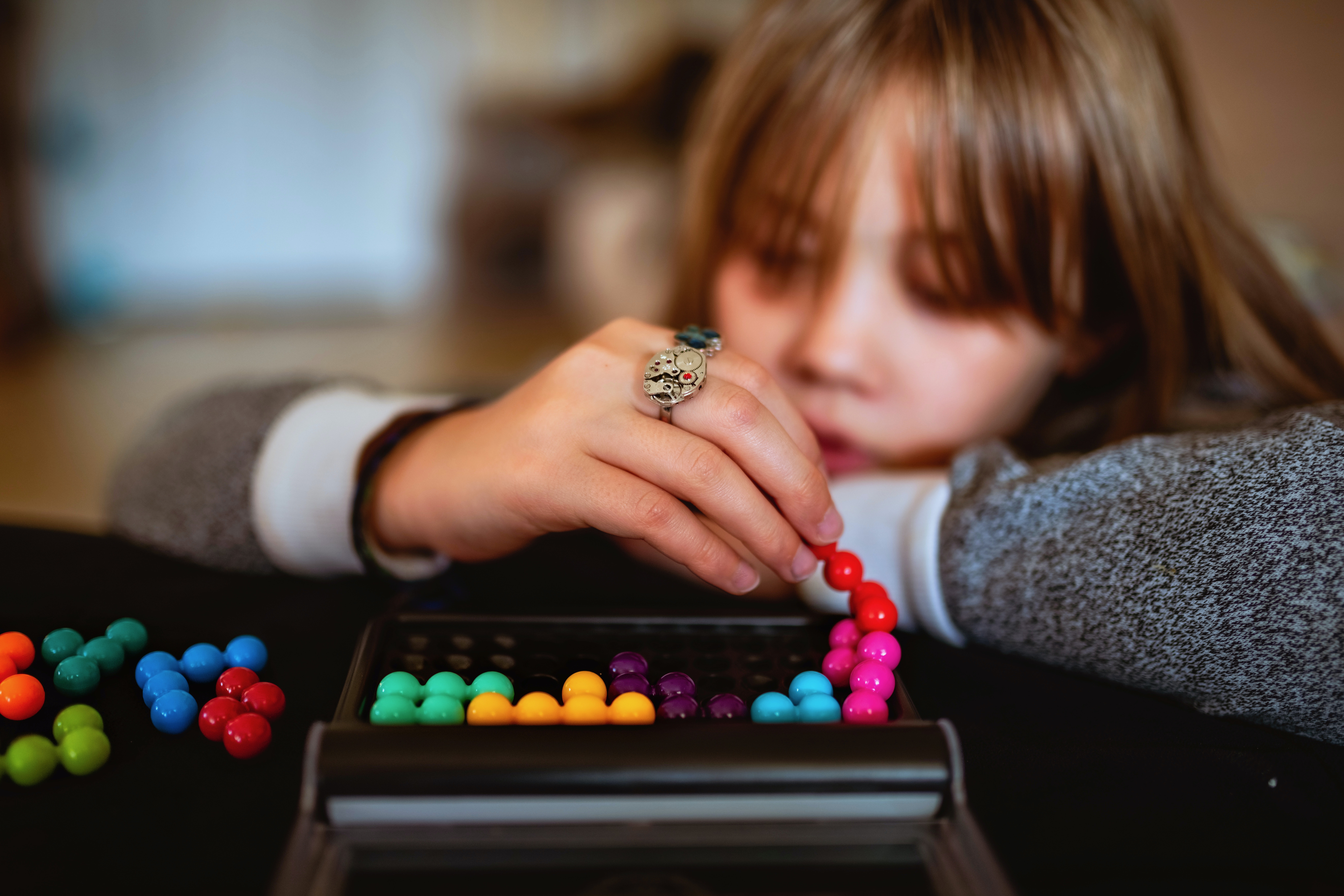 A girl is focusing on a chain of colourful beads.