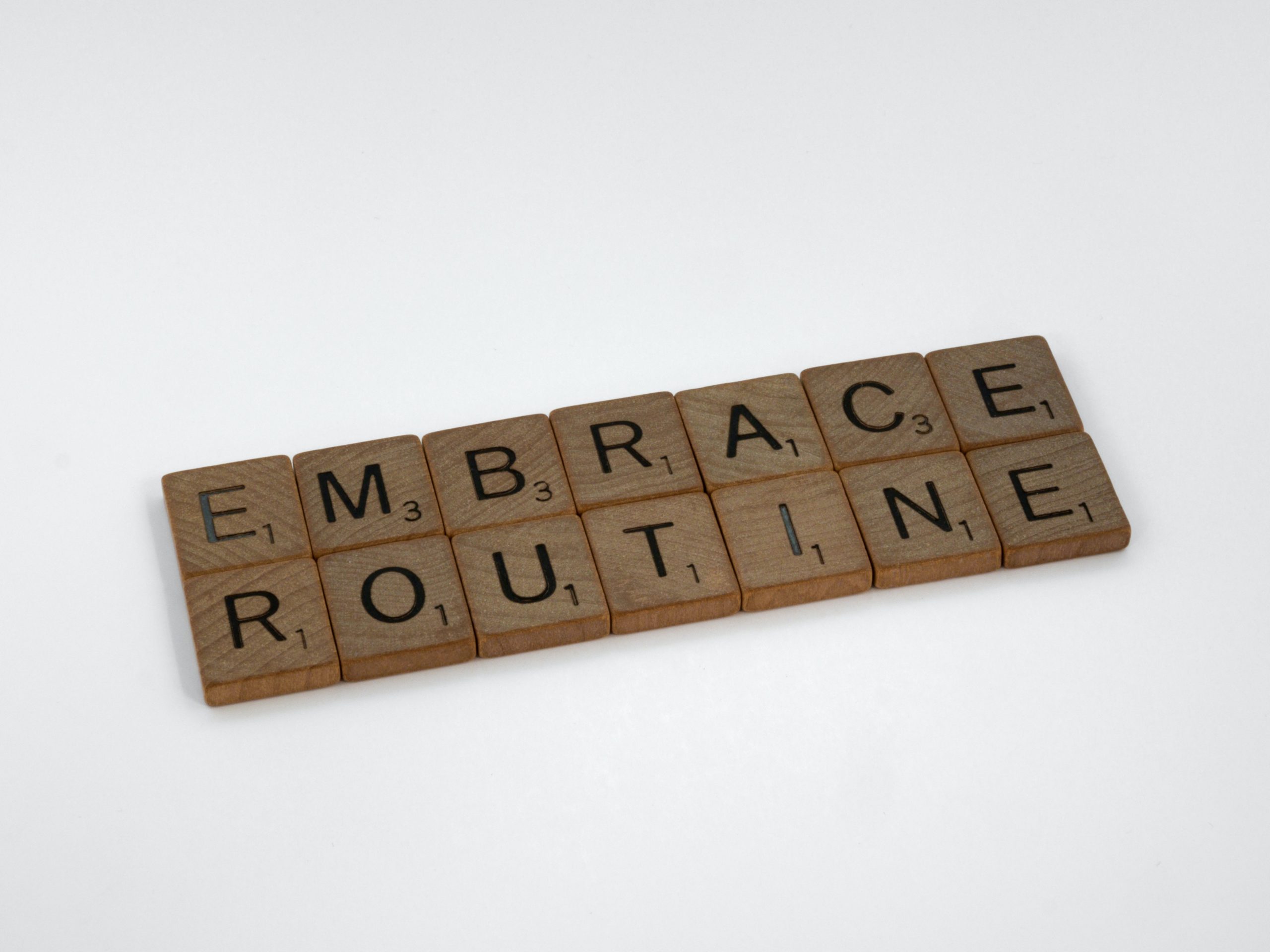 Some wooden Scrabble tiles spell out, "EMBRACE ROUTINE."