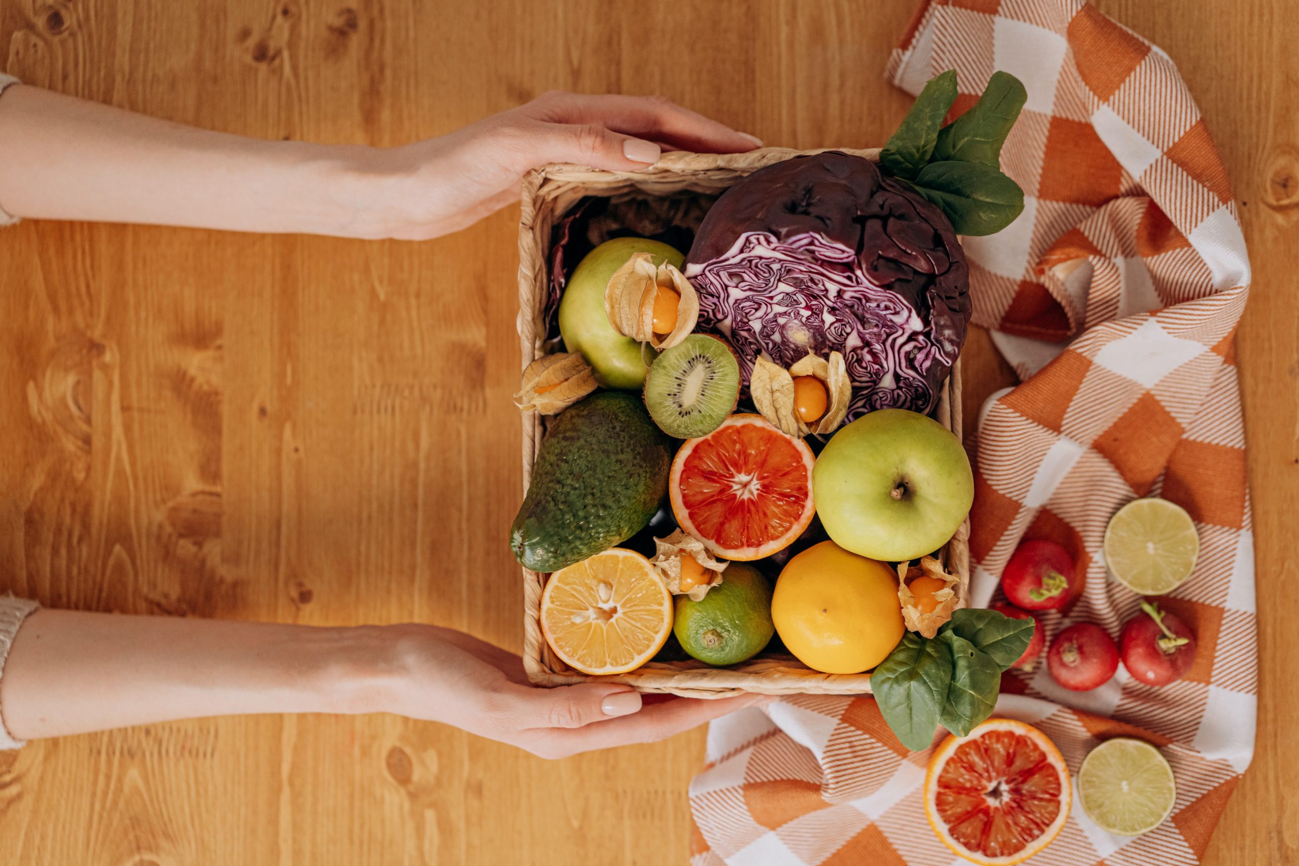 A person's hands are holding a box of fruit and vegetables.