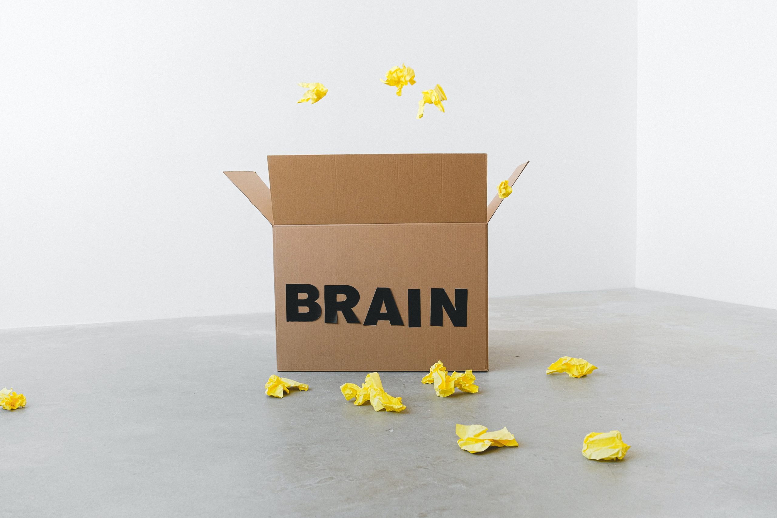Some scrunched up pieces of paper are being thrown into a box with the word, "BRAIN," on it.