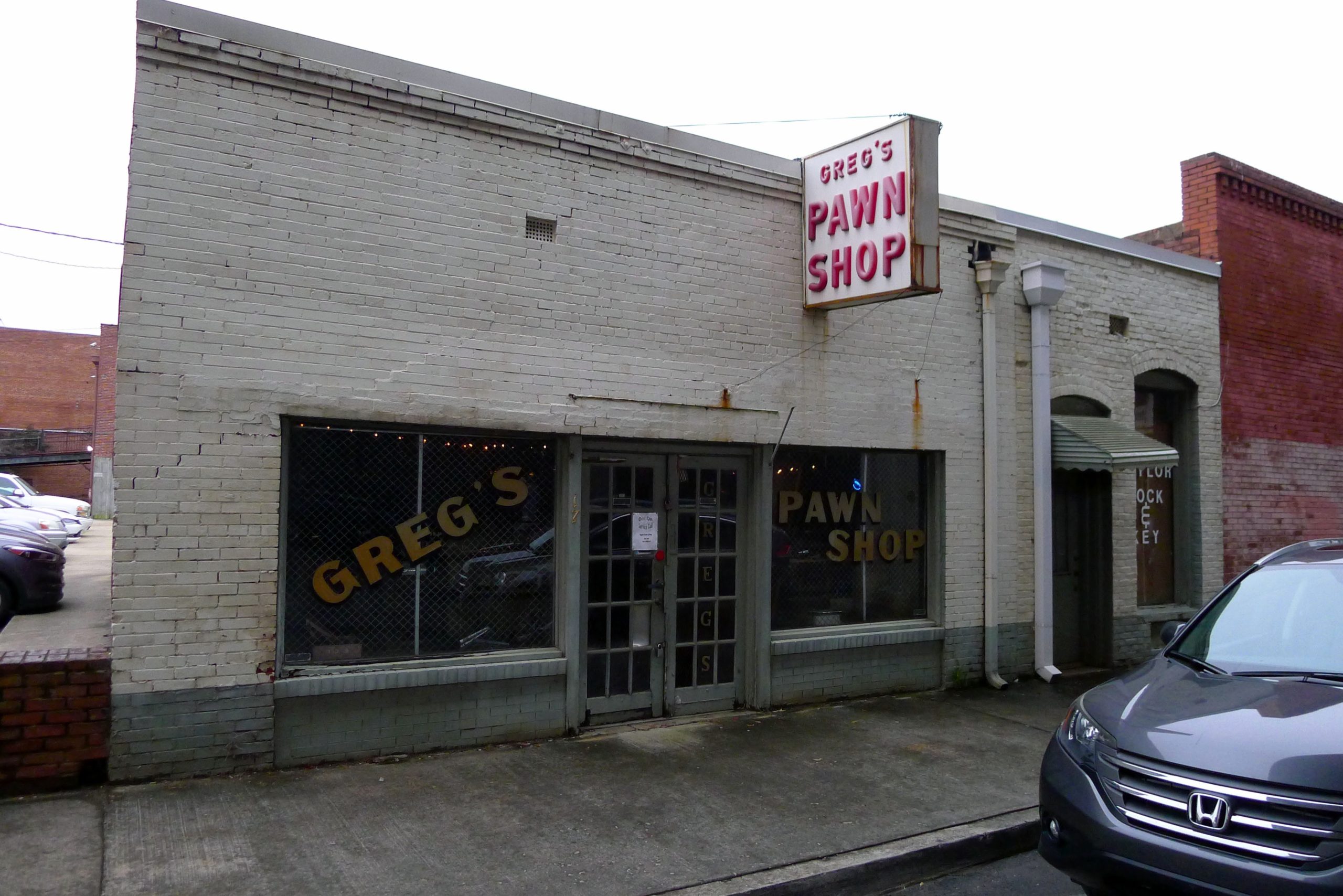 A shop called Greg's Pawn Shop stands in a street.