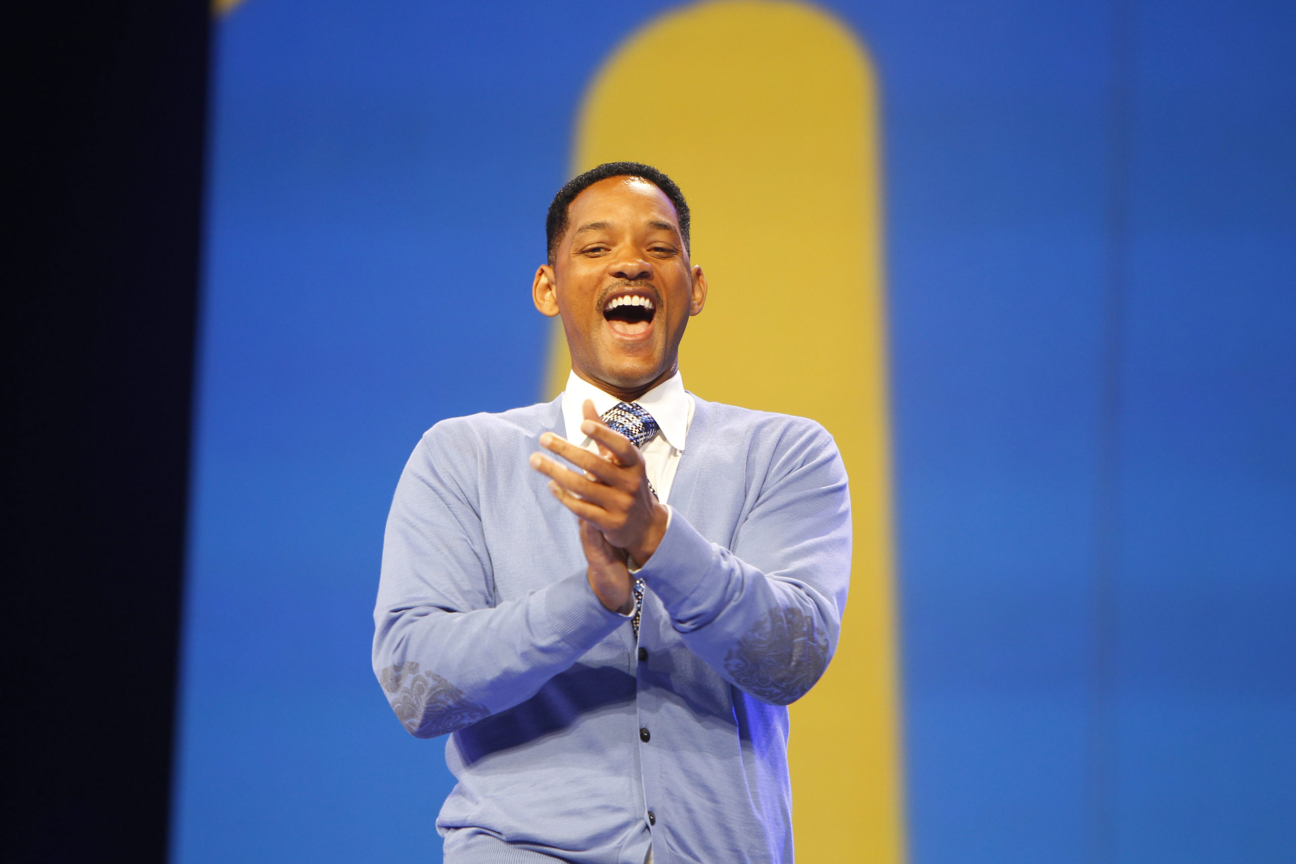 Will Smith is standing in front of a blue and yellow wall.