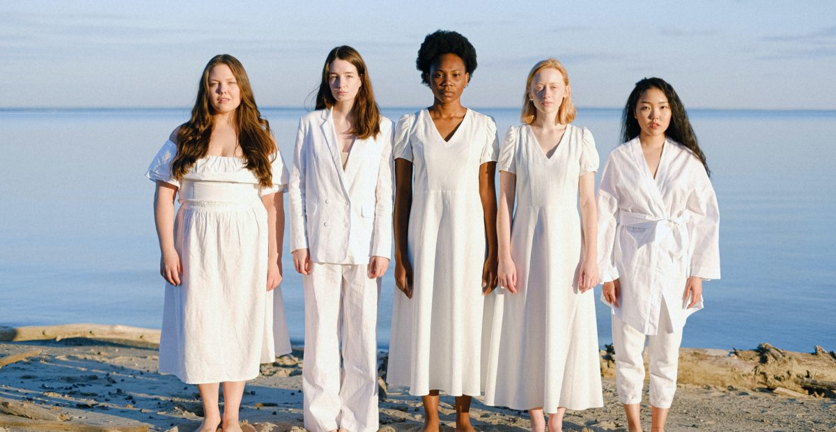 A diverse group of women stand on a beach.