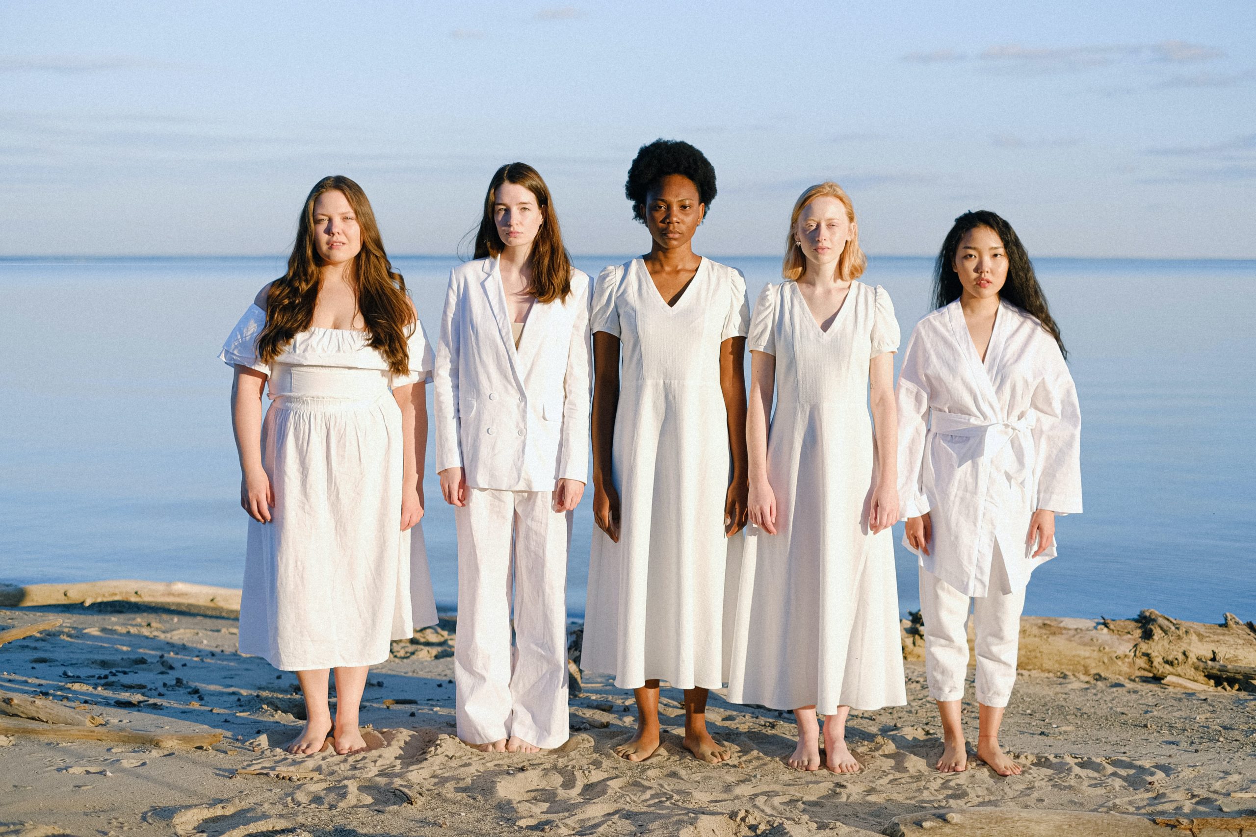 A diverse group of women stand on a beach.