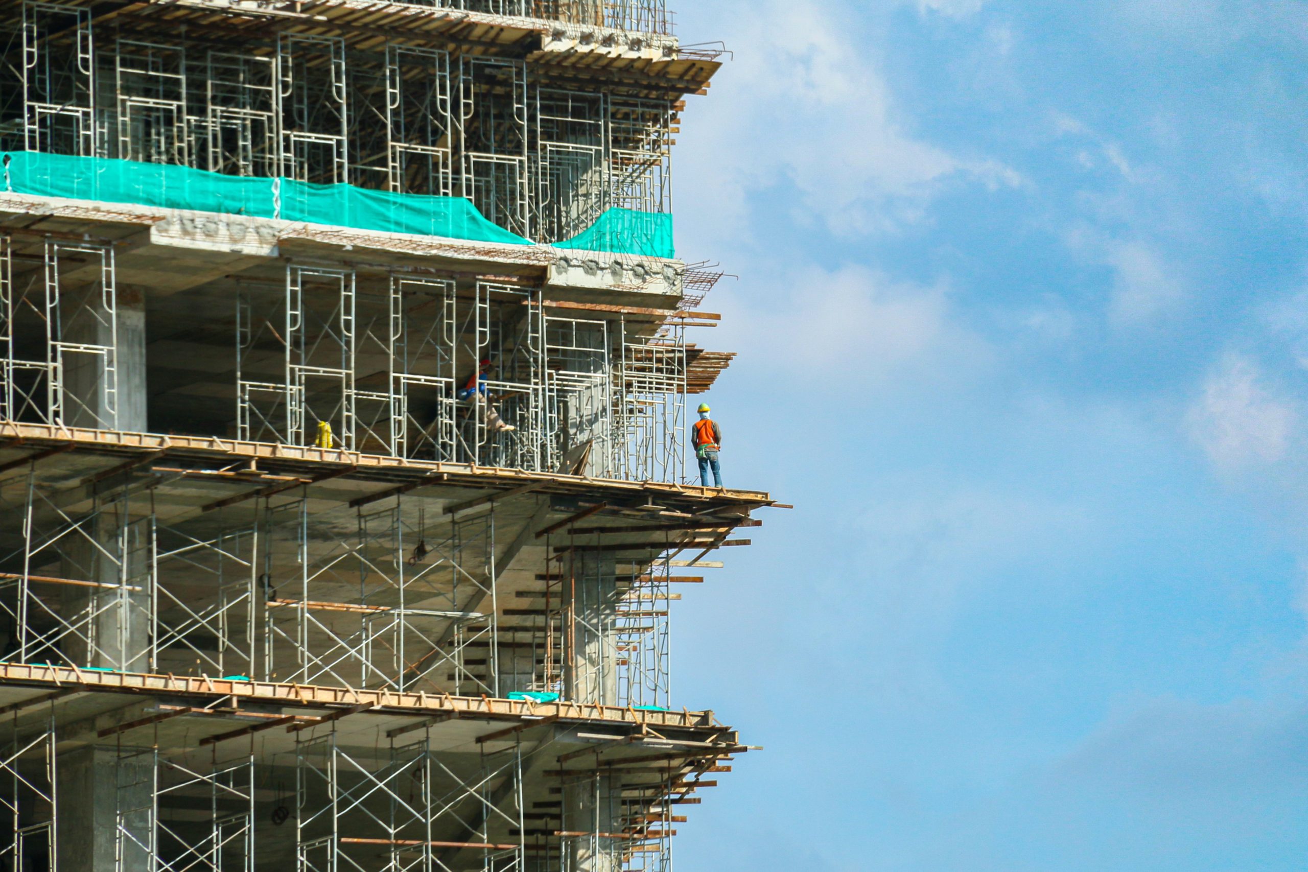 A construction worker is standing on scaffolding that is surrounding a building site.