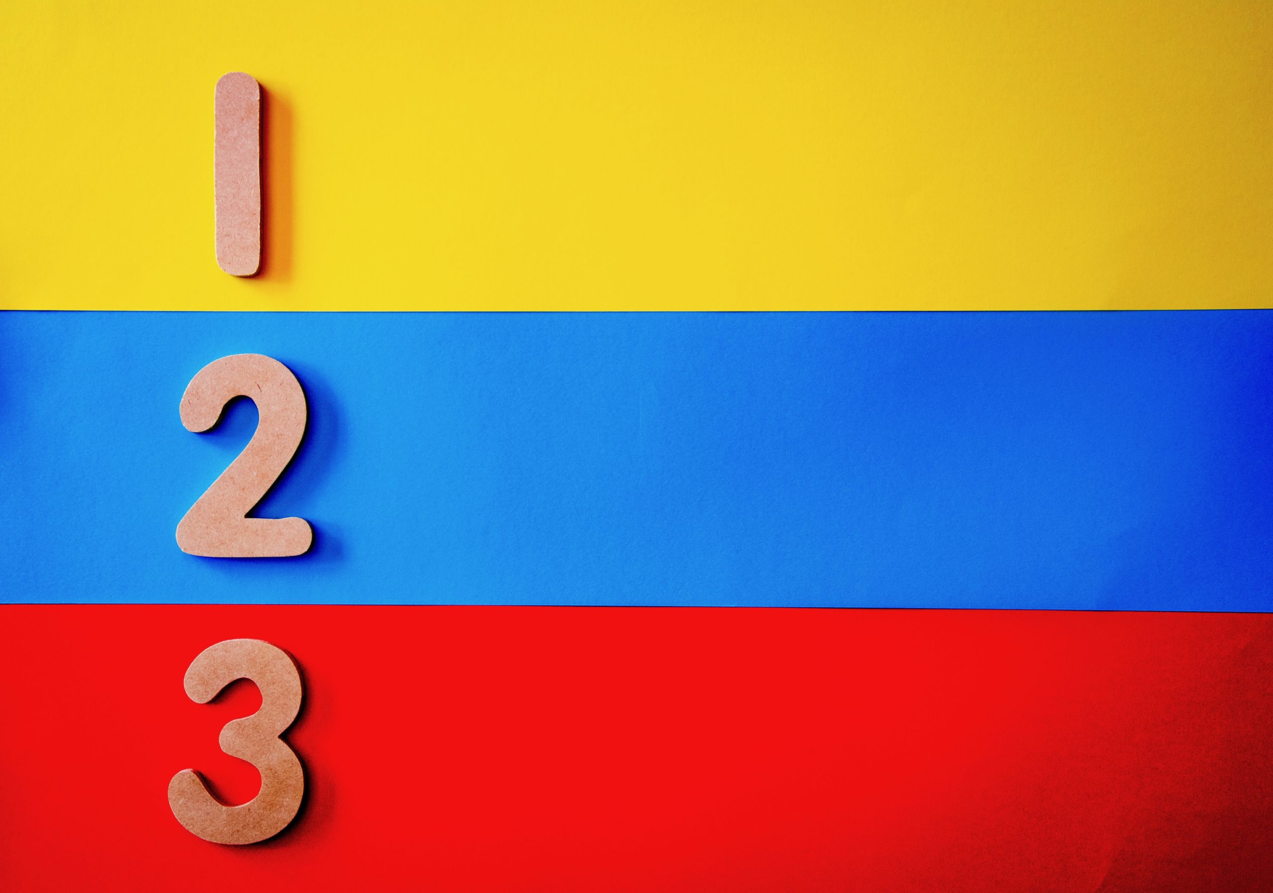 The wooden numbers 1, 2 and 3 are lying on a striped yellow, blue and red background.