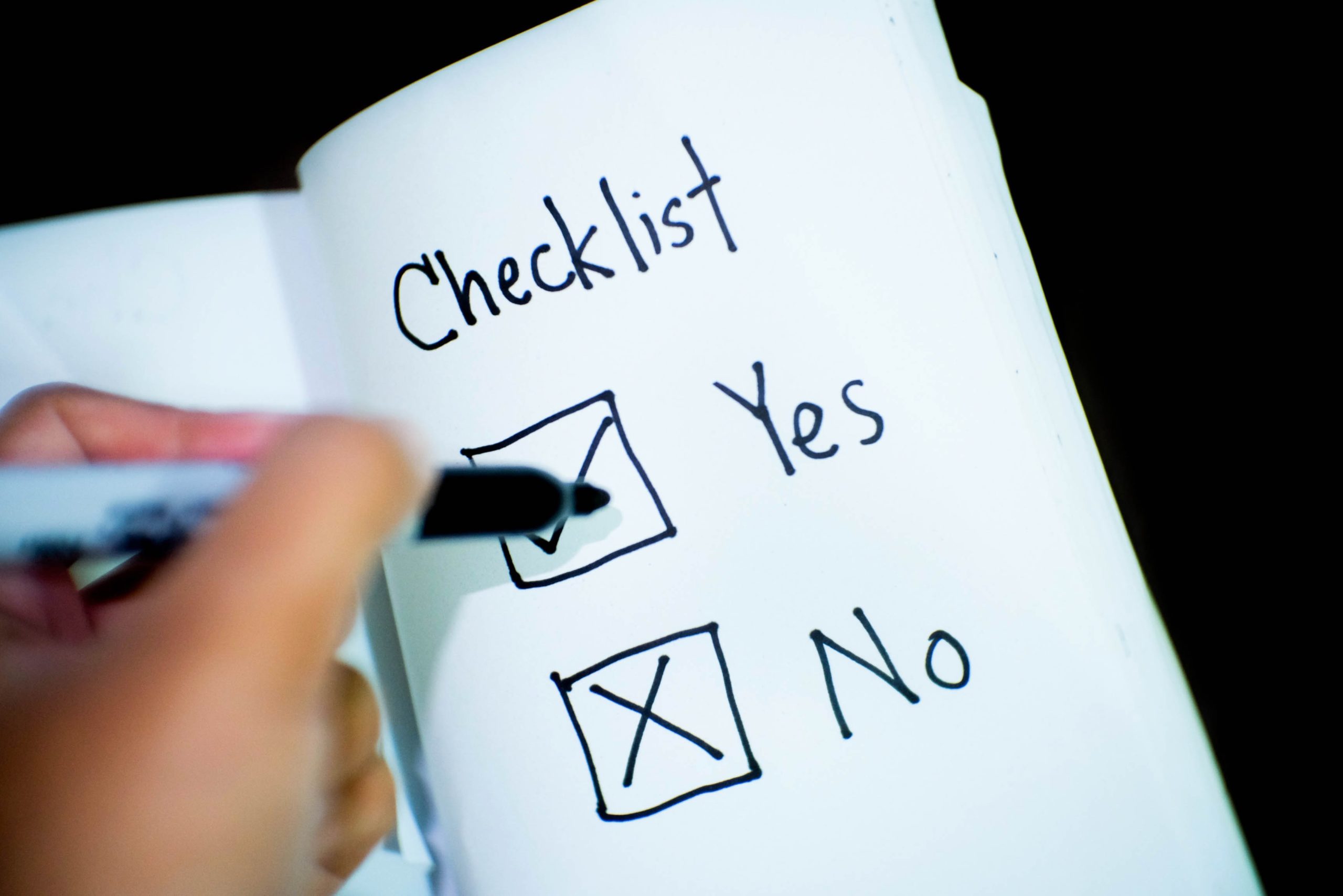 An open book with a checklist on one page. There is a tick next to Yes and a cross next to No. A hand holding a pen is on the tick.