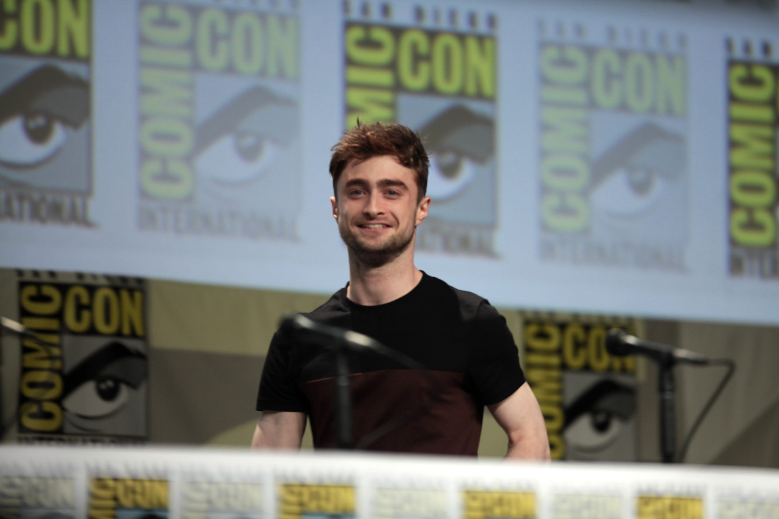 The actor Daniel Radcliffe is speaking on a panel at a Comic Con event.