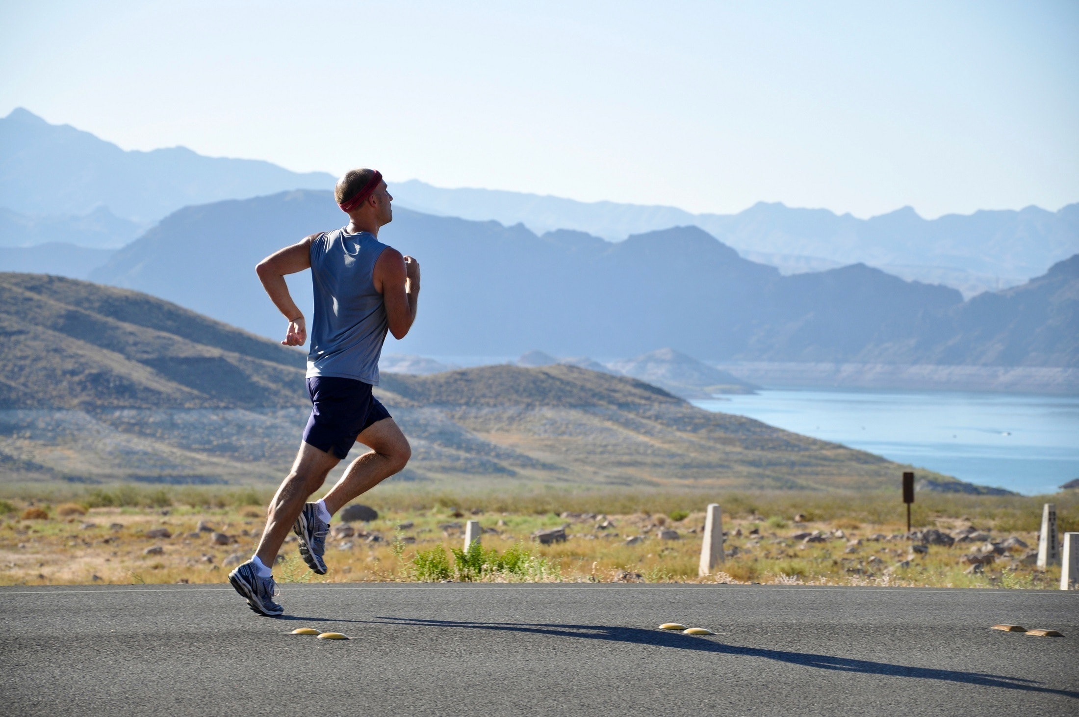 A man is running past a lake and some hills.
