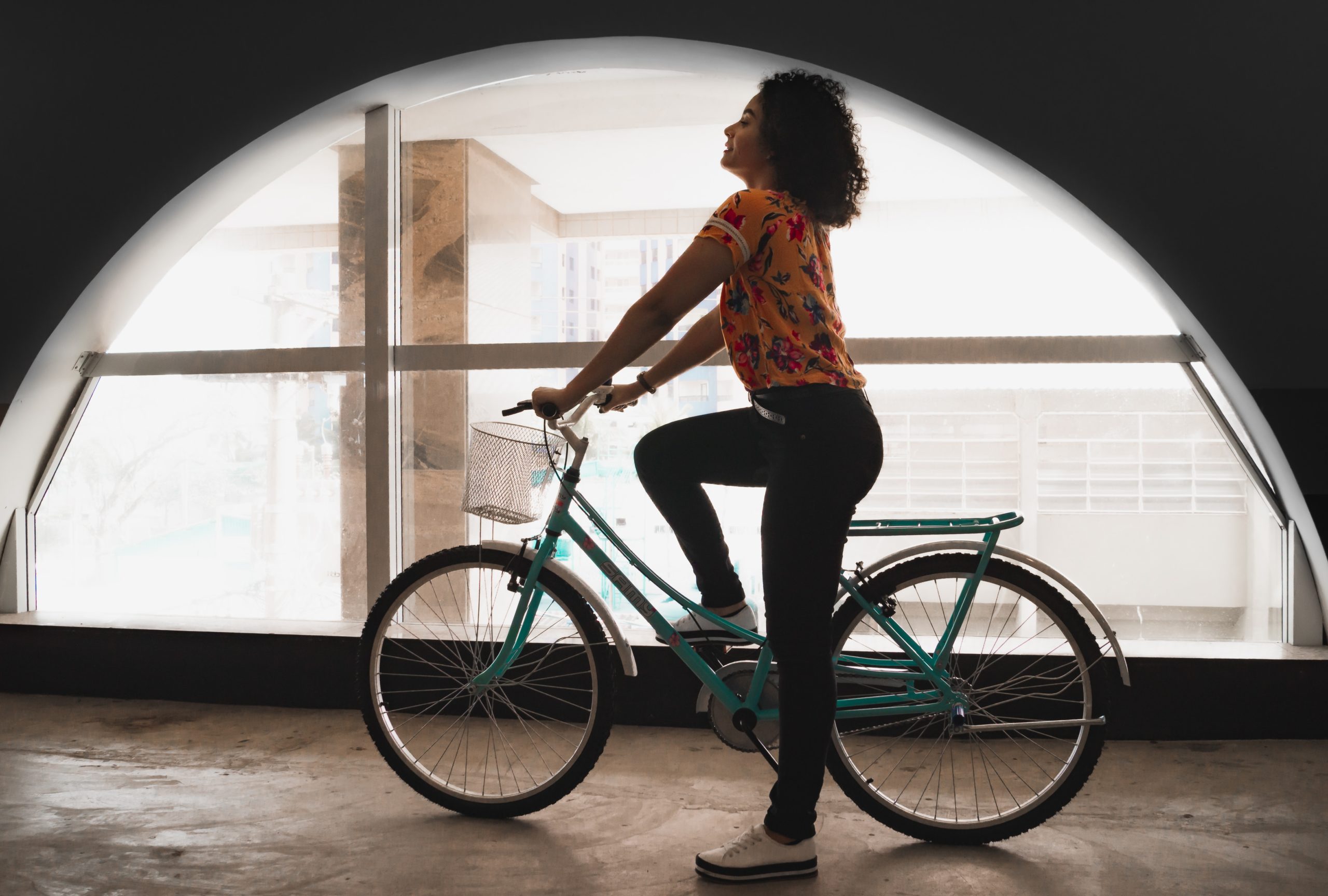 A woman is riding a bicycle past a semi-circle-shaped window.