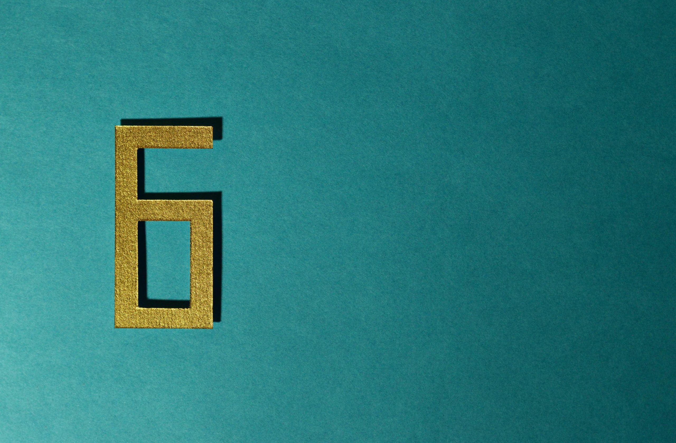 A golden rectangular number 6 lies on a teal surface.