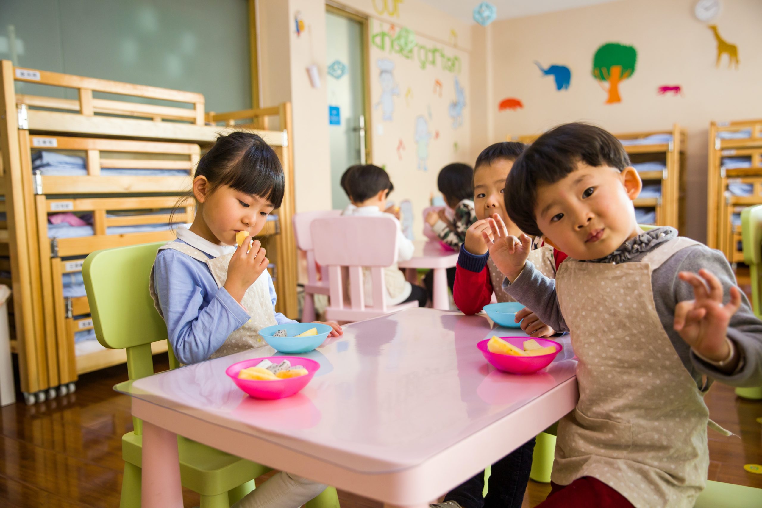 Some pre-school children eat snacks at a table.