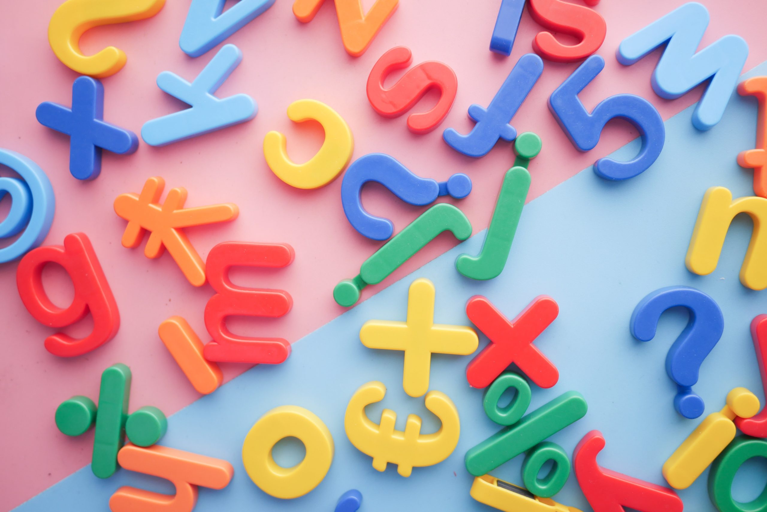 Several coloured magnetic letters, numbers and symbols lie on some pink and blue paper.