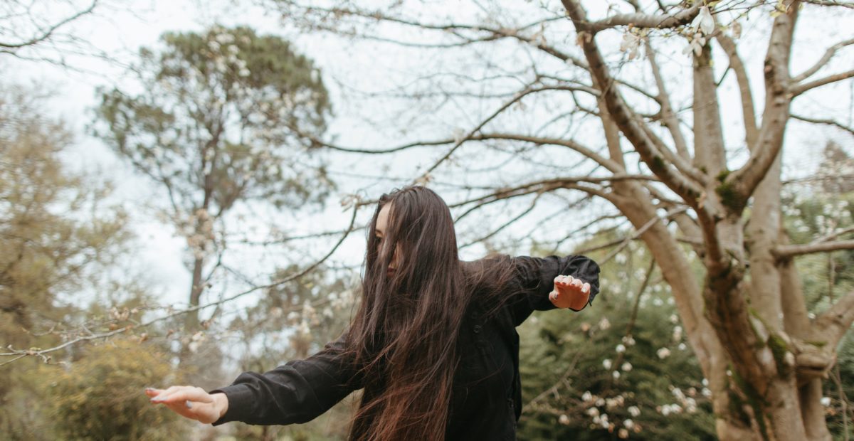 A woman is dancing in front of some trees.