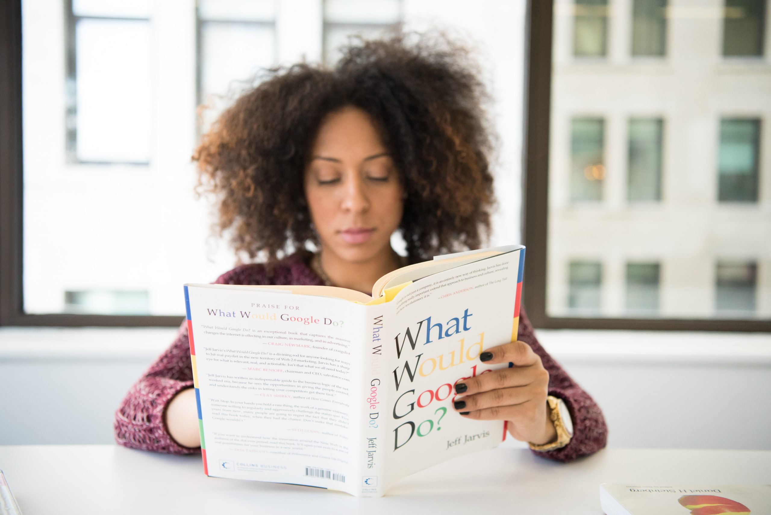 A woman is reading a book called What Would Google Do?