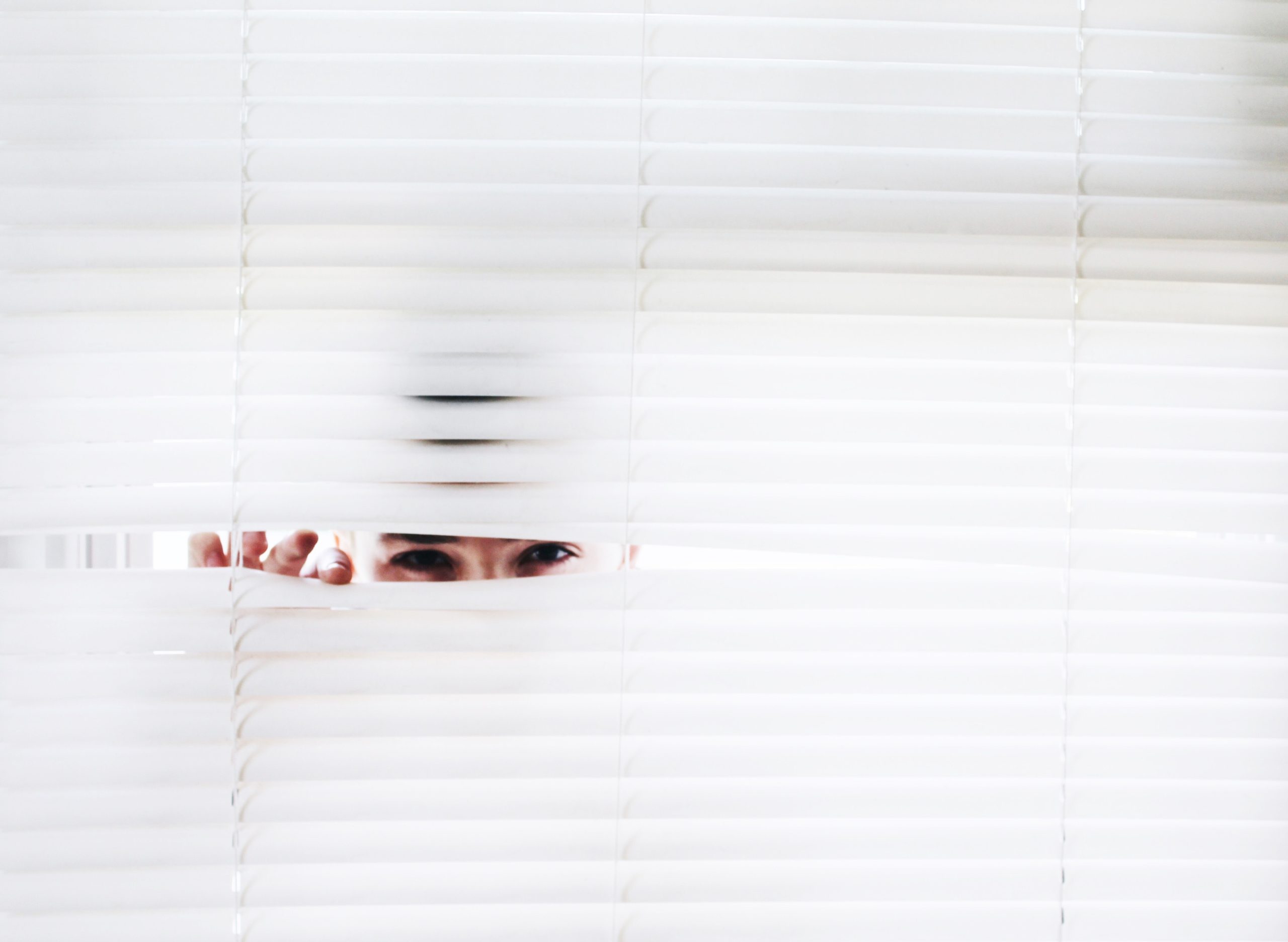 A person is hiding behind some window blinds.