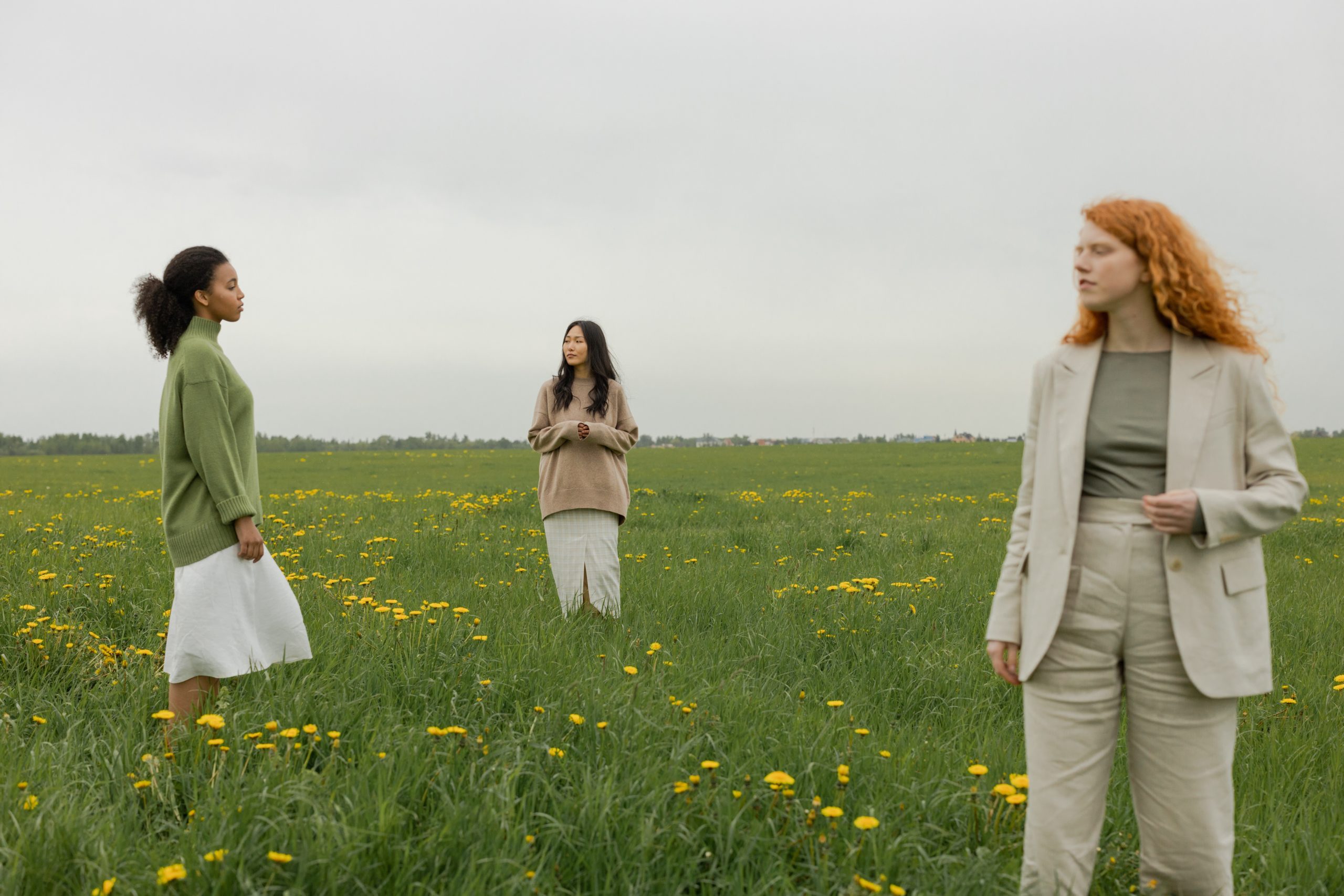 Three diverse women are standing apart from each other on some grass.