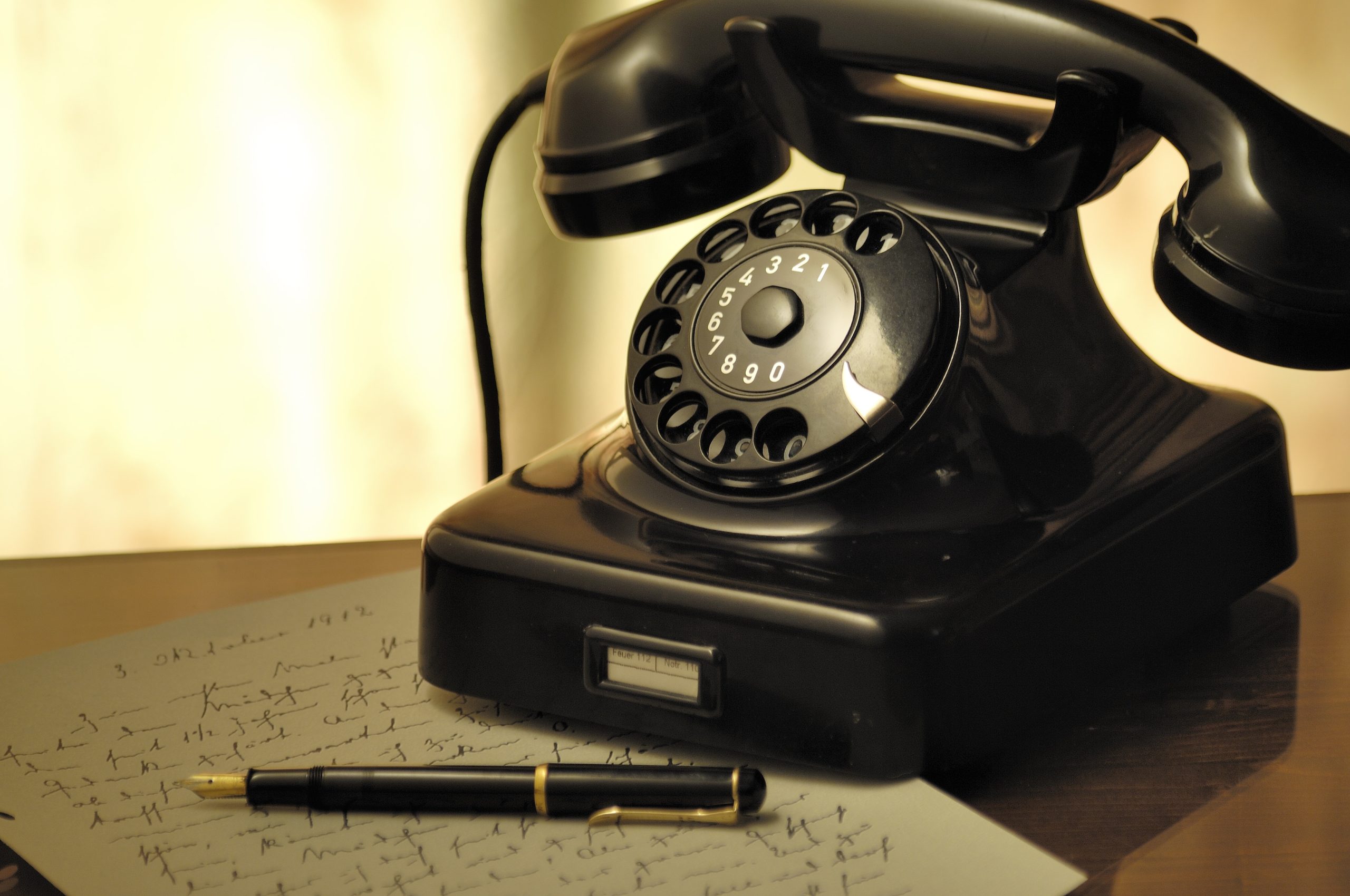 An old-fashioned rotary telephone sits on a table alongside a sheet of paper and a pen.