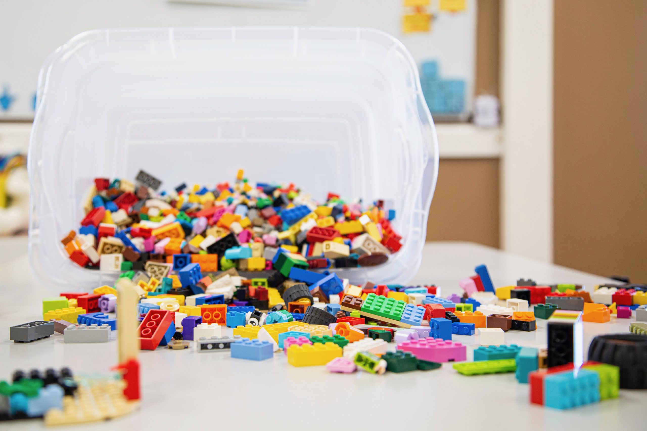 A plastic storage box is tipped over. Lots of Lego bricks are pouring out of the box.