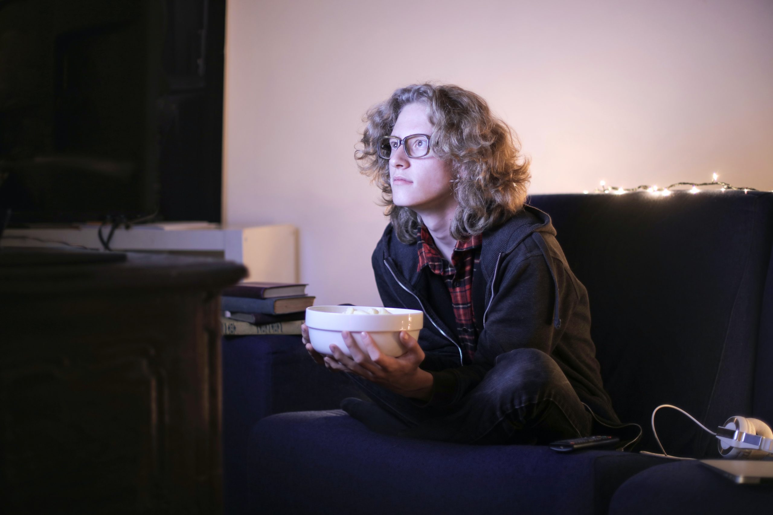 A young man is watching a film on TV. He is holding a big bowl of popcorn.