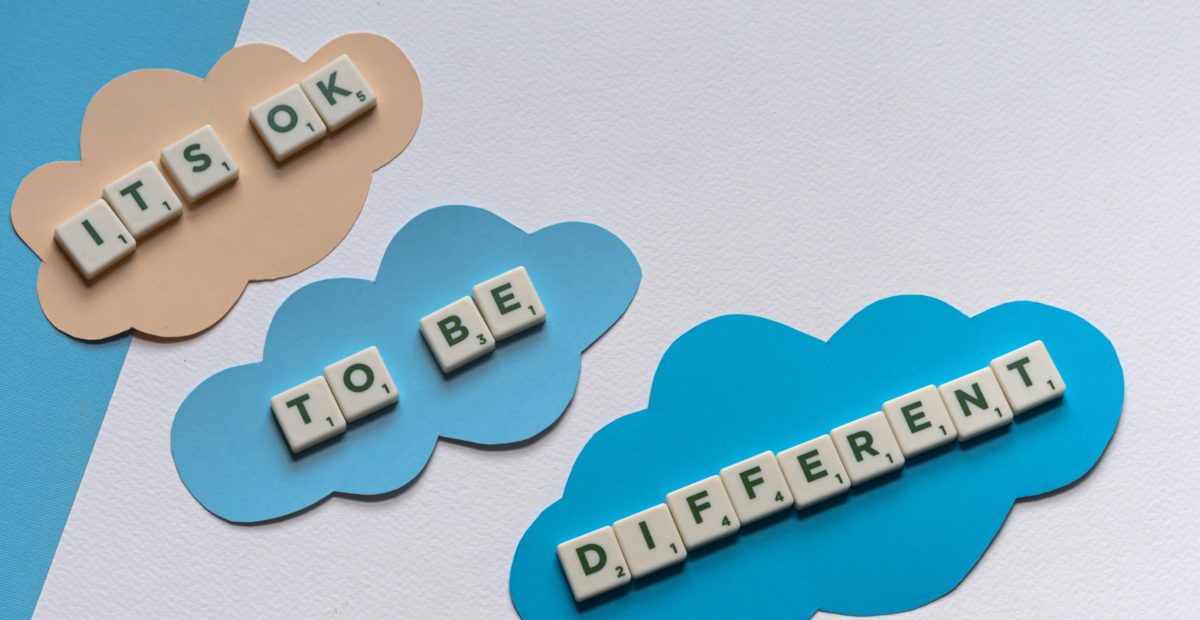 Some Scrabble tiles that spell, "It's OK to be different," lie on some coloured paper clouds.