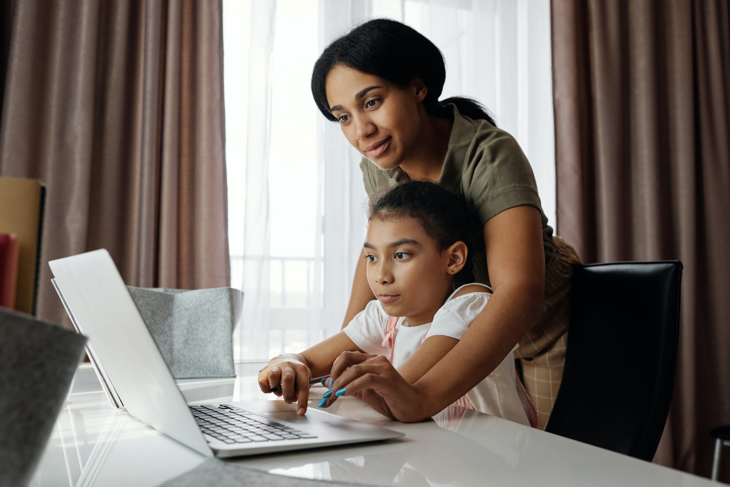 A mother and her daughter are using a laptop.