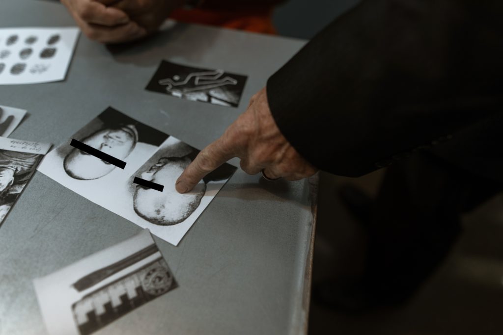 A detective is pointing to a photo of a suspect on a table.