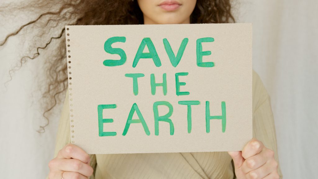 A woman is holding up a sign that says, "Save the Earth."