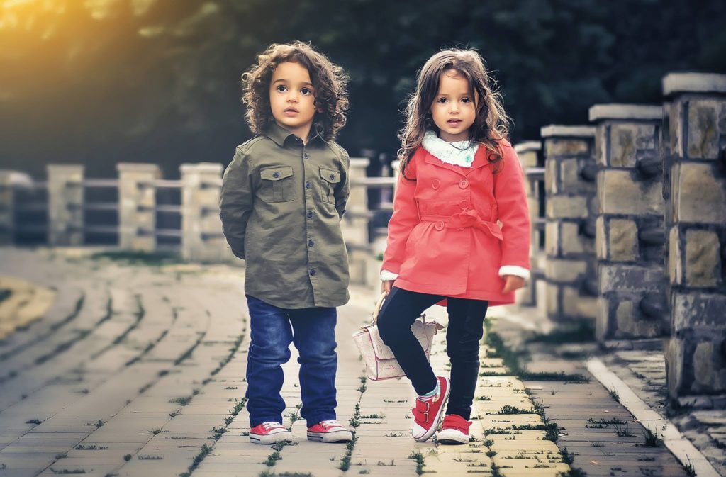 A boy and a girl are standing on a pavement.