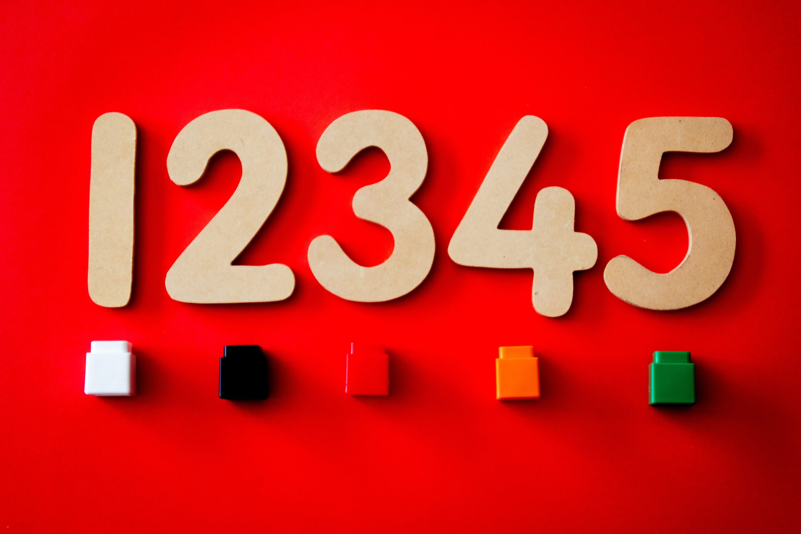 Some wooden numbers and coloured plastic blocks are lying on a red surface.