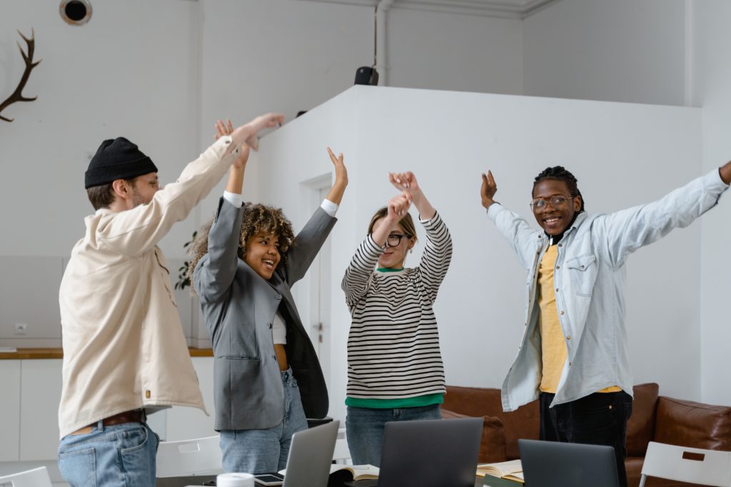 A group of adults in business-casual clothing are lifting their arms up in the air.