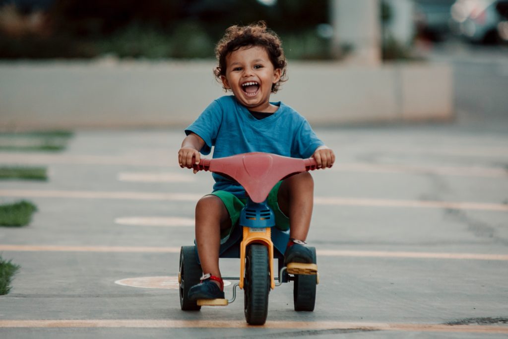 A young boy is smiling and riding his tricycle.