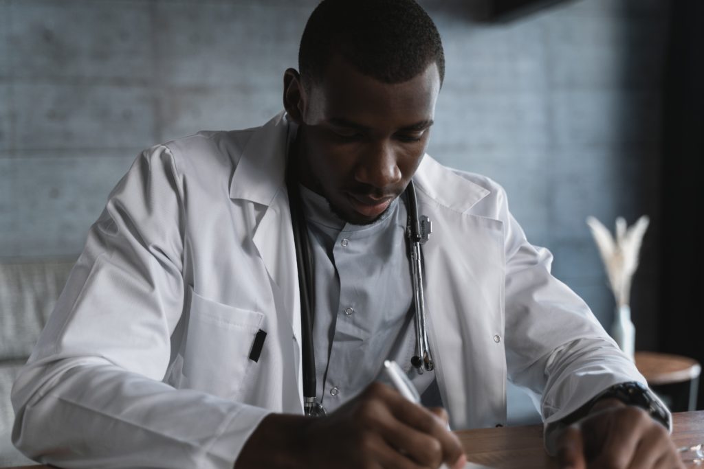 A male doctor is looking down as he writes on a piece of paper.