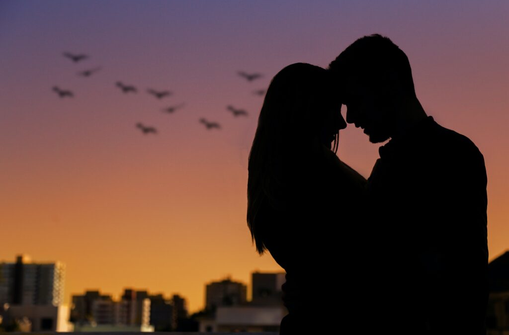 Silhouettes of a couple embrace against a sunset sky.