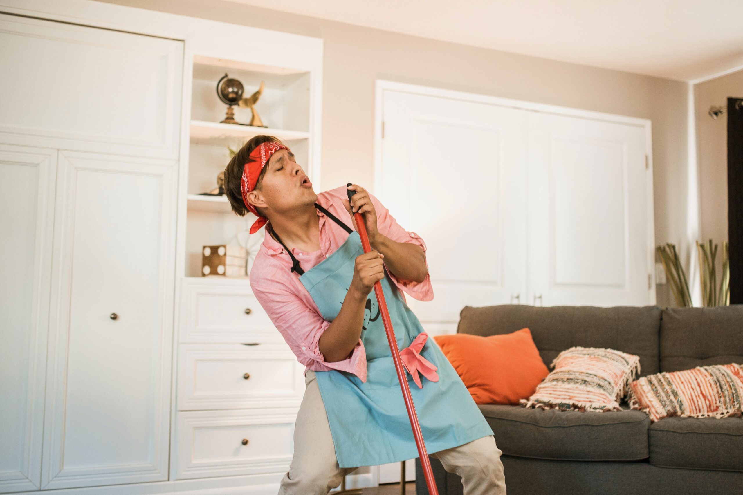 A man is holding a broom or mop handle and singing into it.