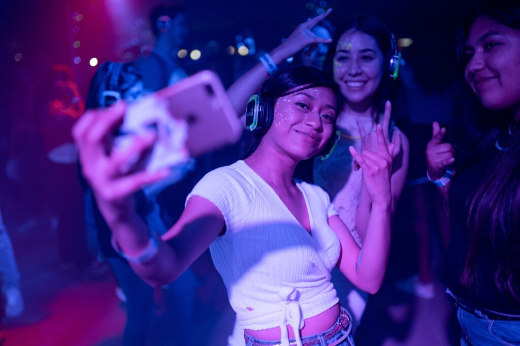 A young woman photographs herself and her friends on her phone at a silent disco.