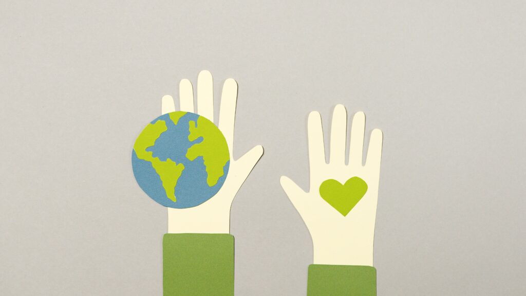 Cut-out paper artwork of 2 hands. Planet Earth is on one hand and a green heart is on the other.