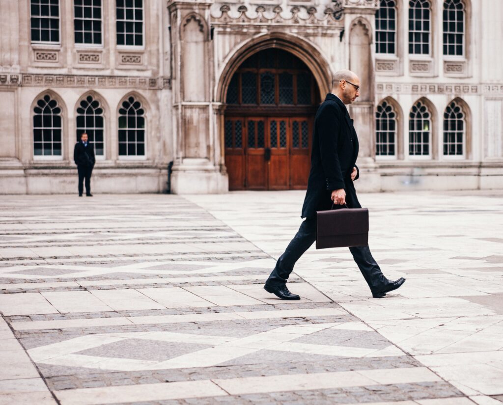 A man in a suit walks down a street whilst carrying his briefcase.