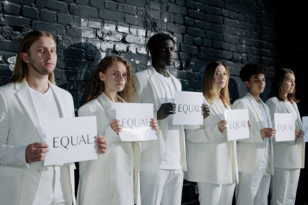 Several people in white suits hold up signs that say, "EQUAL."