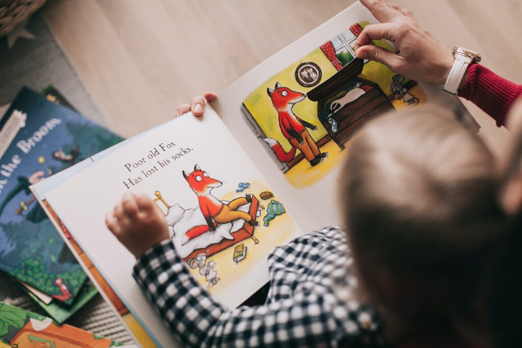 Close-up of an open picture book that an adult is reading to a child.