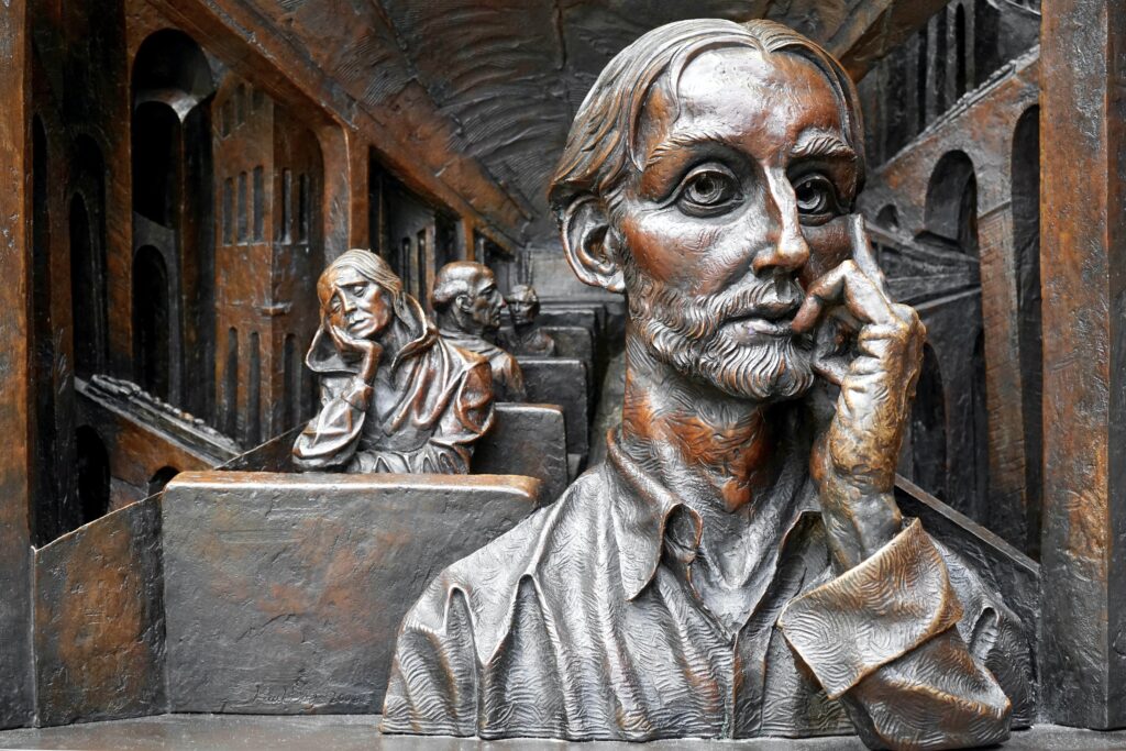 Bronze-like artwork of several people sitting on a train. The man and the woman who are the most visible at the front look anxious.