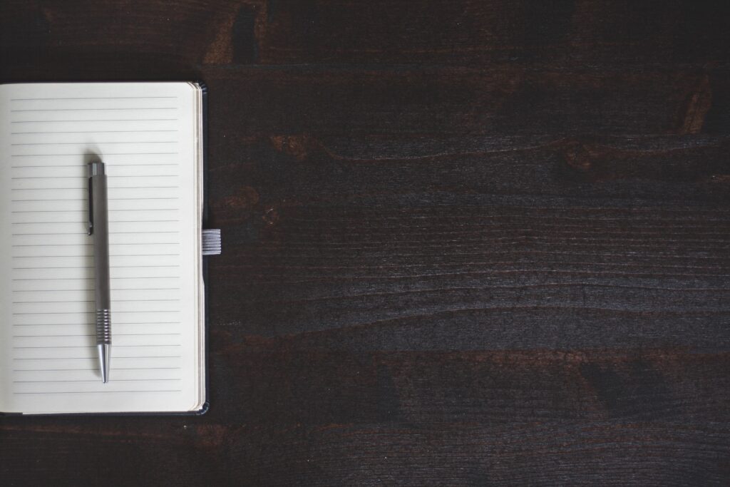 An open notebook and a pen lie on a black wooden surface.