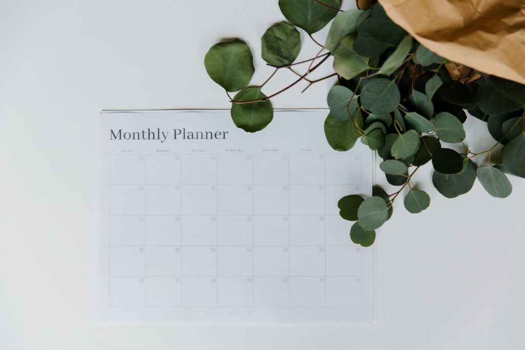 A monthly planner is stuck on the wall. A plant appears in the foreground.