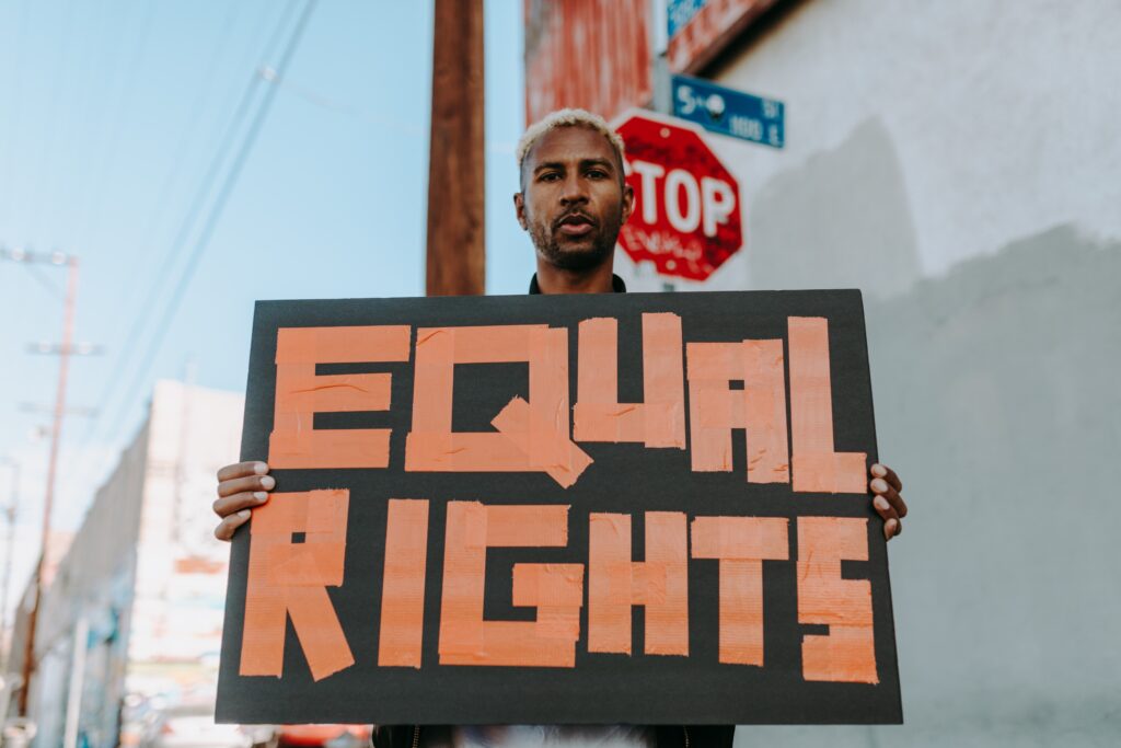 A man stands in a street and holds up a sign that says, "EQUAL RIGHTS."