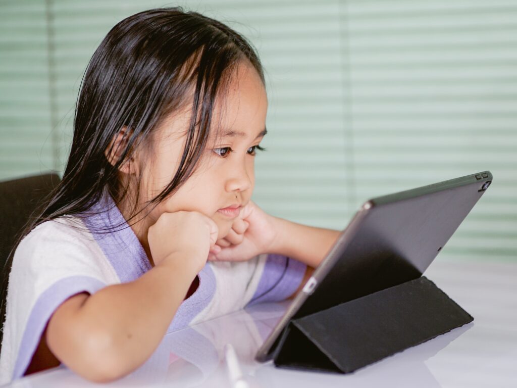 A girl is looking at her iPad. She has her fists clenched underneath her chin.